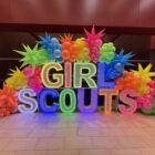 colorful Girl Scouts balloon display with neon rainbow balloon garland, startburts and LED letters by Balloon Boutique